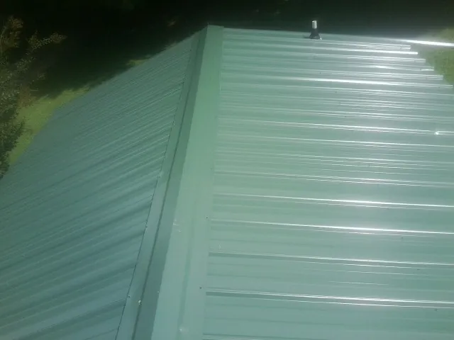 New green metal panels meeting at the ridge of a roof — Flat Roof Repair work by our crew in Flat Rock