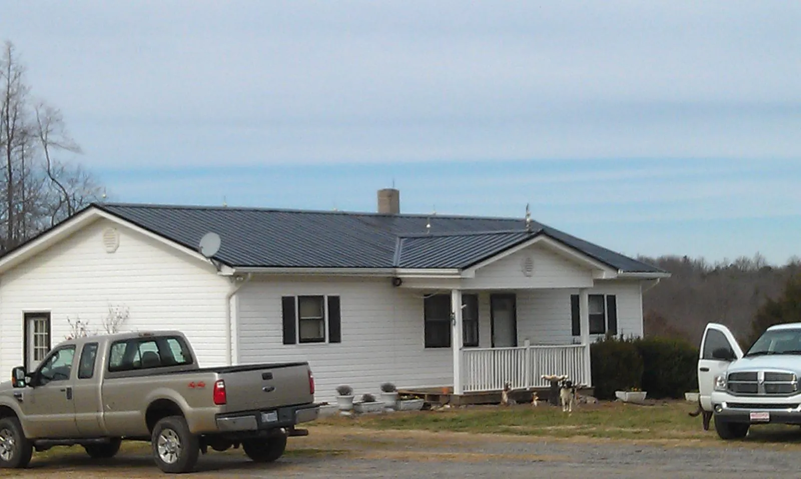 Finished dark metal roof on a white ranch home with work trucks parked in Flat Rock